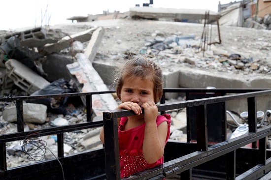 a young girl holds a railing outside her family’s partially destroyed home, in the Shejaiya neighbourhood of Gaza City. 